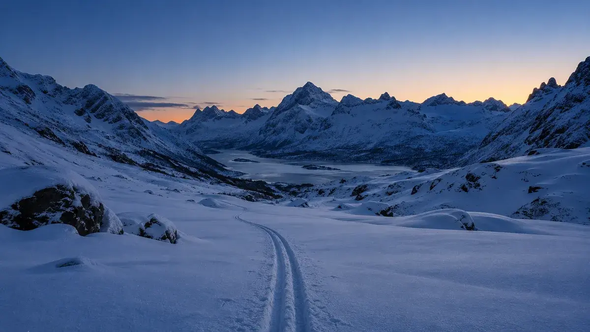 Ferskt skispor gjennom en fjelldal i blåtimen før soloppgang, med tinder som så vidt får morgenlys